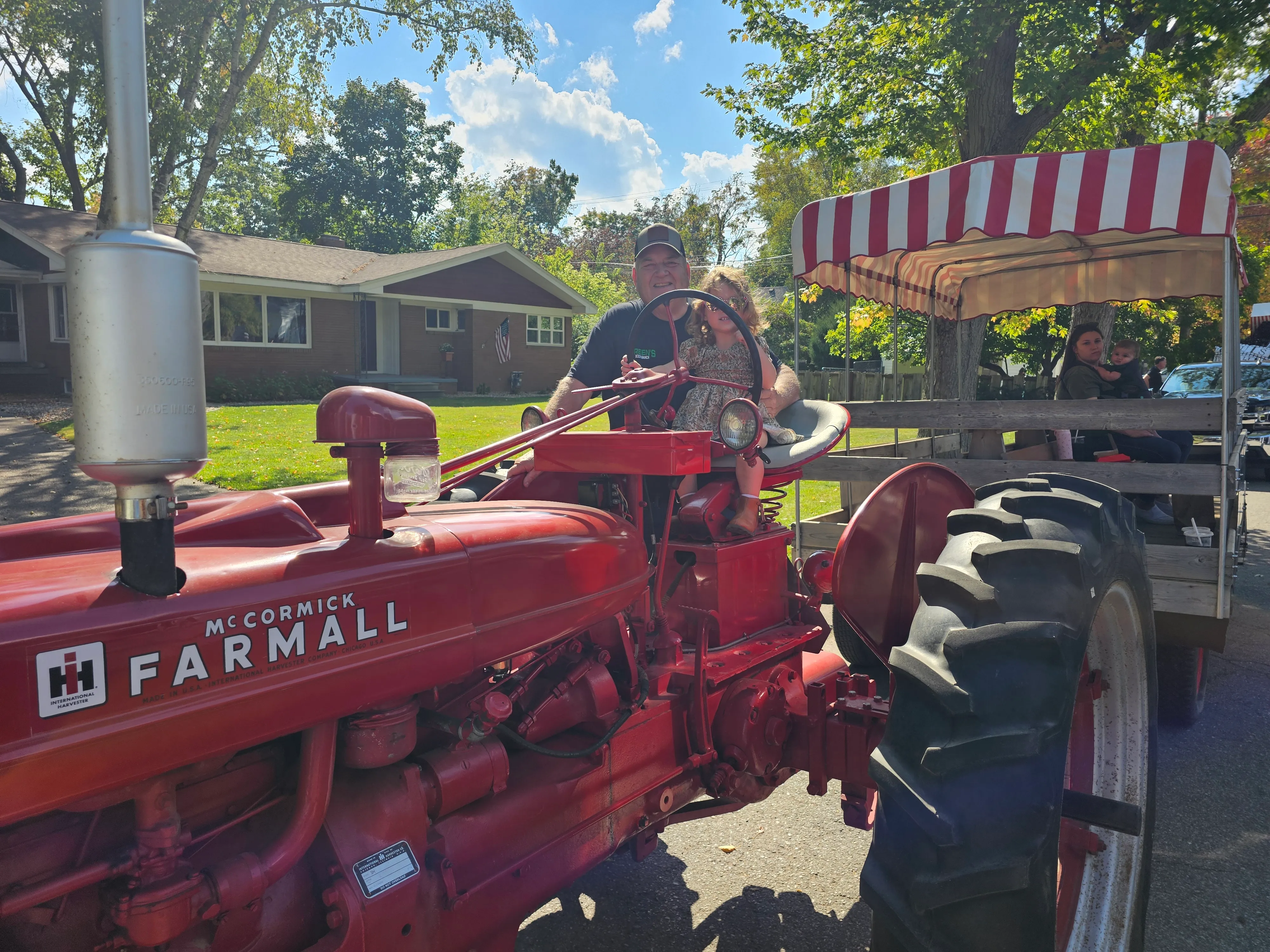 A vintage red McCormick Farmall tractor pulling the red-and-white striped hay wagon with visitors seated inside, about to head out on the tour loop