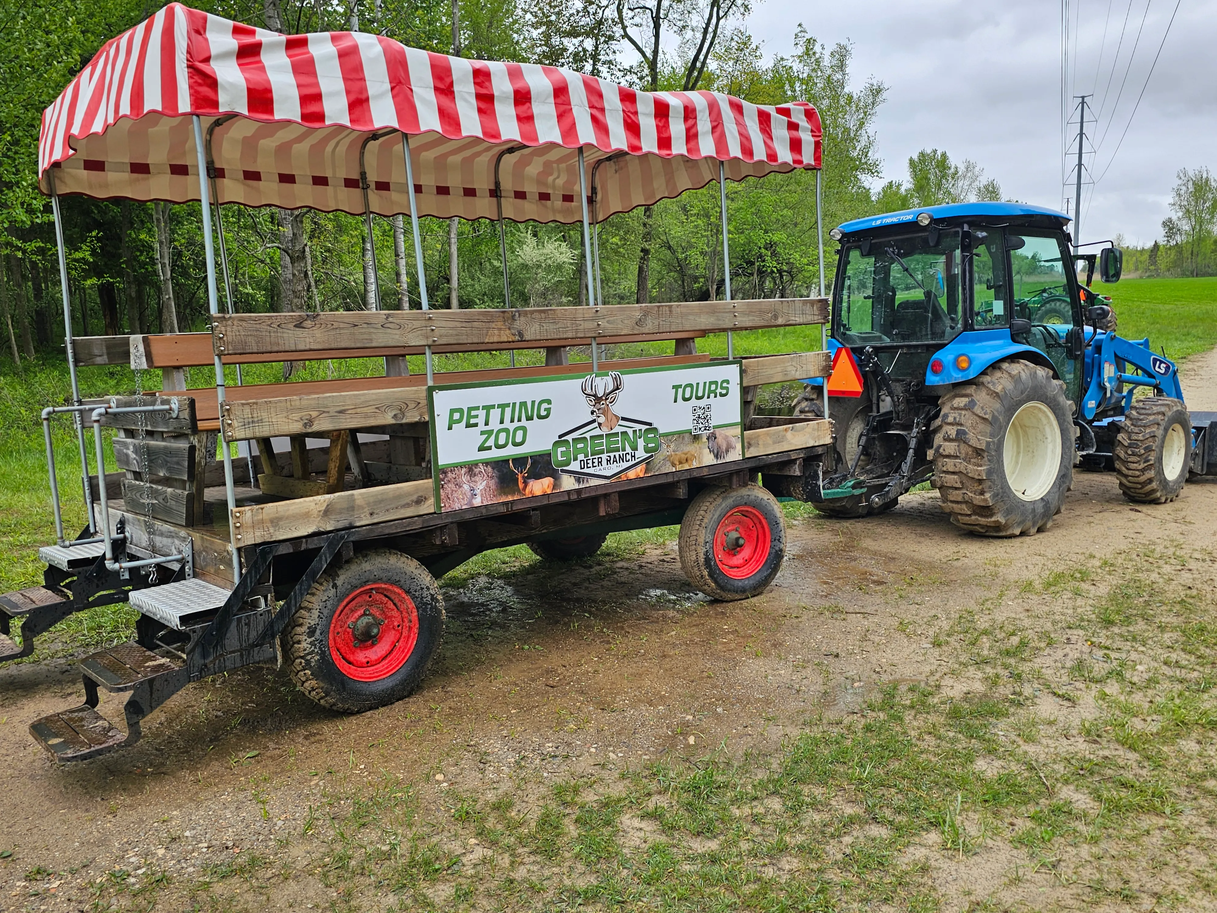 The Green's Deer Ranch petting zoo and tours wagon, branded with the ranch logo and hitched to a blue tractor, parked at the trailhead
