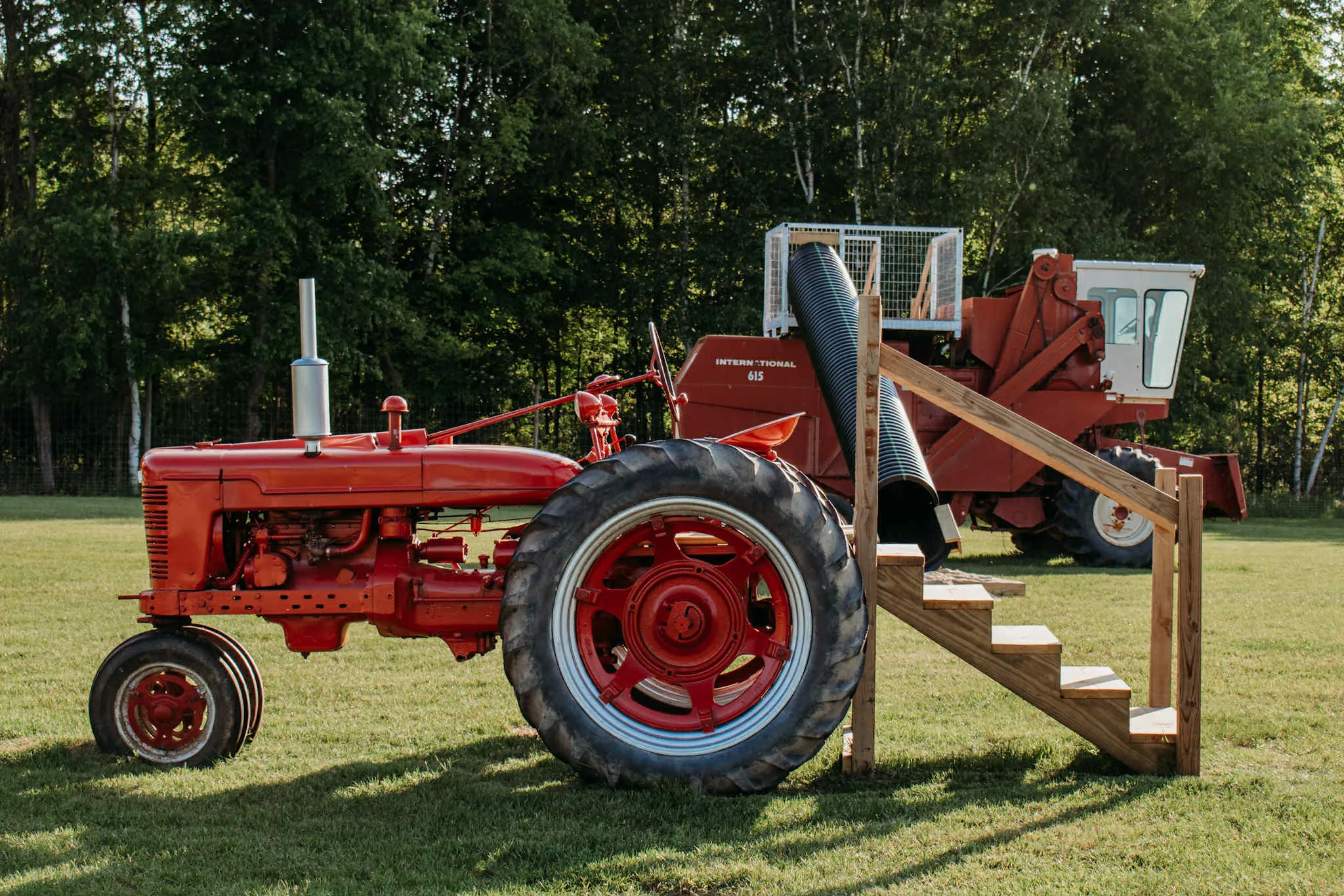 A vintage red McCormick Farmall tractor with wooden steps, next to a retired combine turned climber