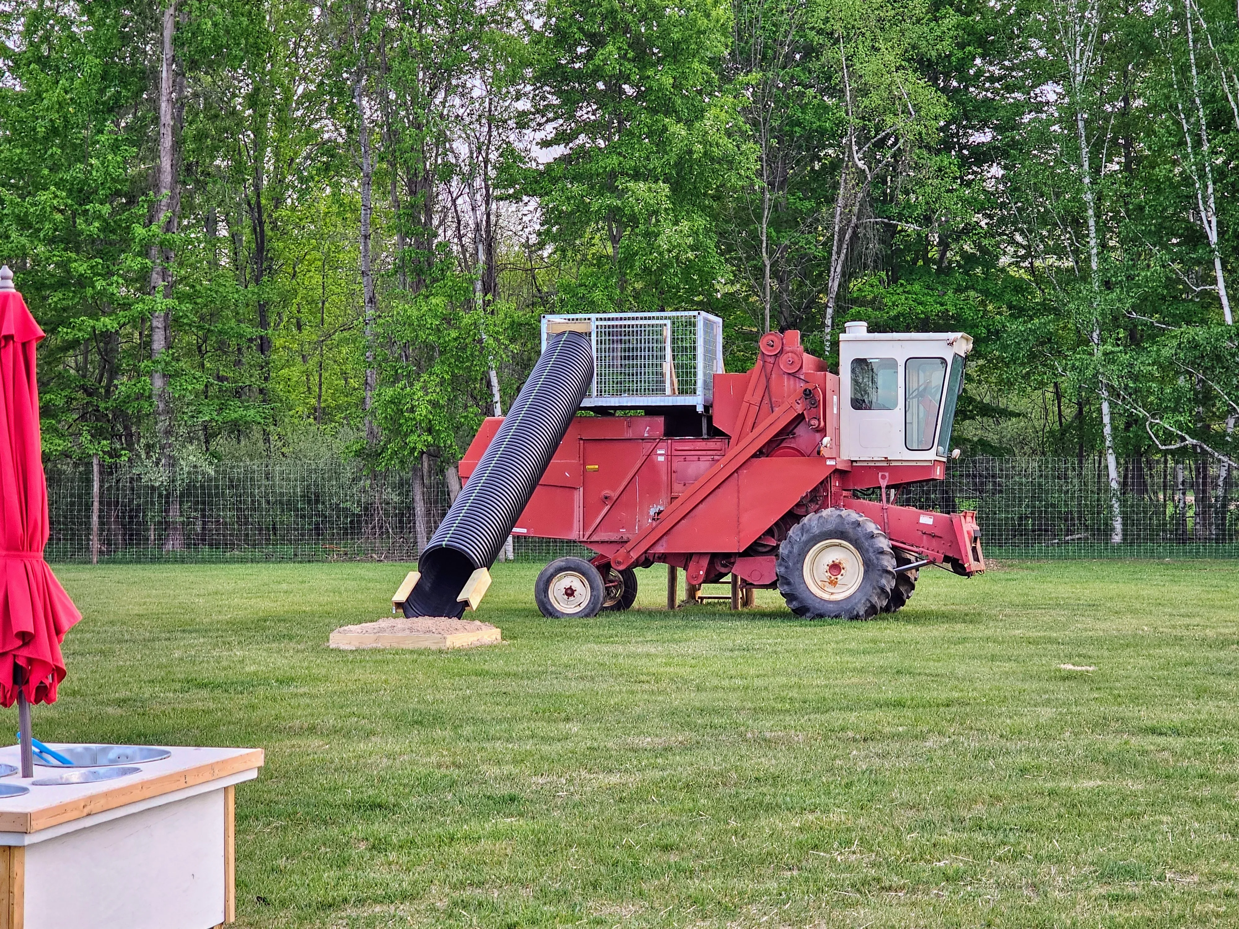 A retired red combine harvester repurposed as playground equipment, with a corrugated chute slide